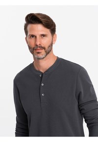 Maglietta Henley a maniche lunghe grigio scuro realizzata in tessuto testurizzato, con placca a tre bottoni, scollatura rotonda e maniche aderenti.