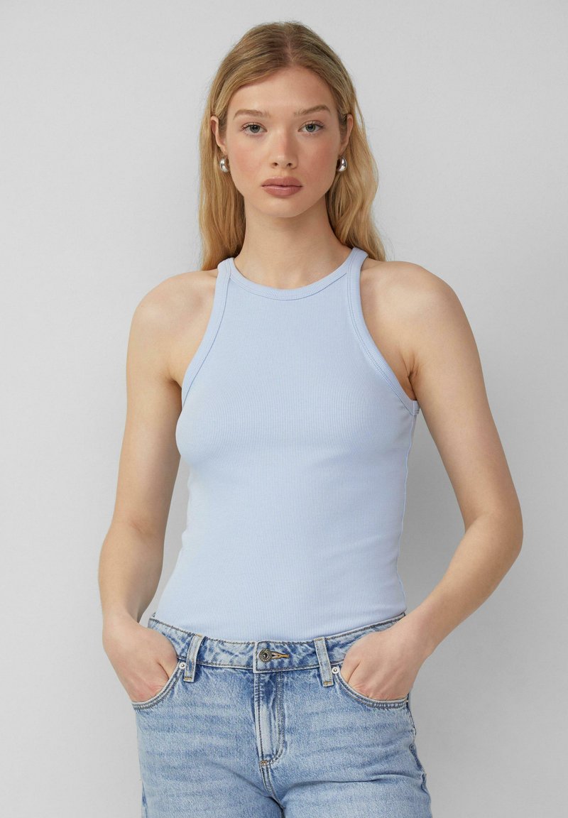 Lichtblauw geribbeld tanktop met hoge hals en mouwloos ontwerp. Model draagt hooghals denim shorts met voorzakken.