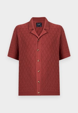 Cardigan en maille couleur rouille à manches courtes avec motif feuilles texturé, boutonnage devant et col ouvert.