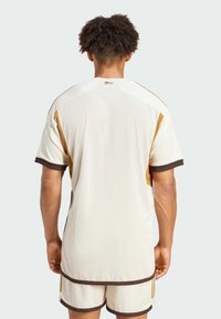 Heren beige sportshirt met bruine afwerking en zijaccenten, voorzien van een textuur stof en een losse pasvorm. Korte mouwen en achterdetails zijn inbegrepen.
