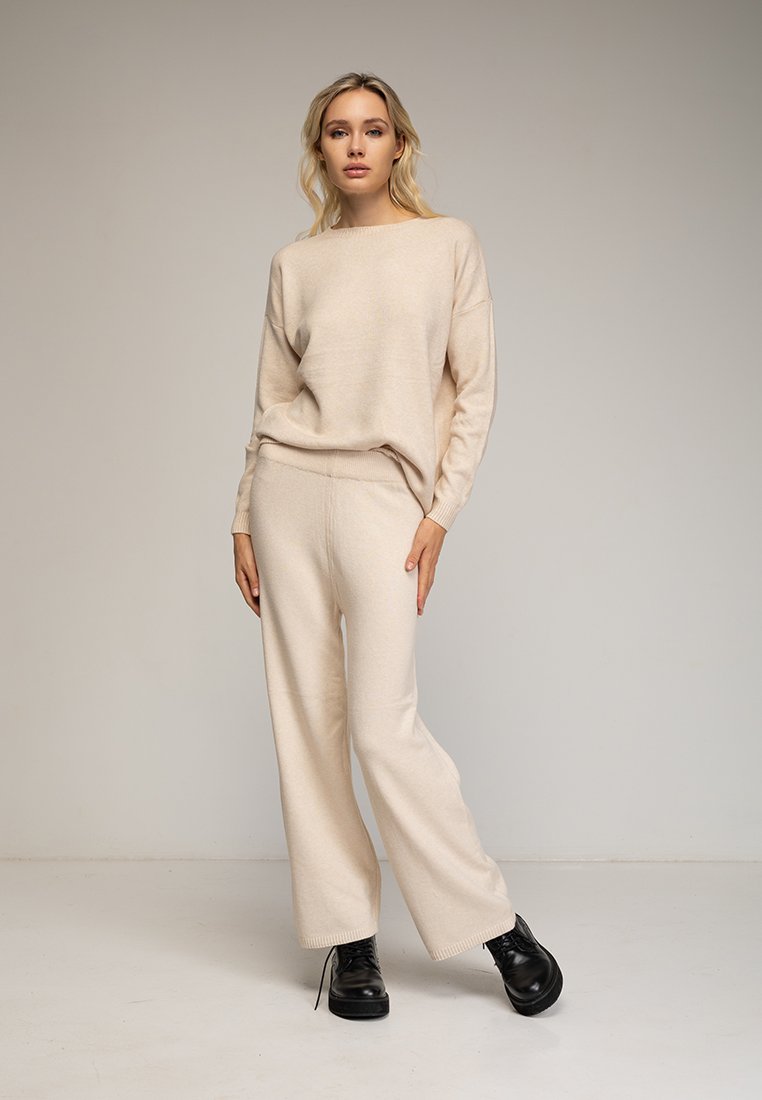 Beige gebreide trui en wijdvallende broek set, met een ontspannen pasvorm, ribgebreide manchetten en een gestructureerde stof. Gescoord met zwarte enkellaarsjes.