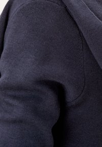 Lähikuva tummansiniseen neuleeseen, jossa näkyy tarkka ompelu ja rakenne taitetussa vaatekätkimessä.