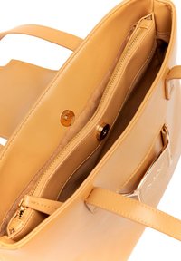 Leren handtas in tan kleur met een gladde textuur. Beschikt over een ritsvak en een magneetsluiting. Het interieur heeft een zachte voering en gouden hardware accenten.