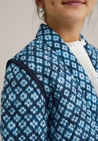 Quiltana jakna v modrem in mornarsko modrem blagu s cvetličnim vzorcem; vsebuje kontrastno mornarsko modro obrobo ob rami.