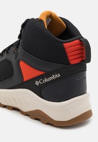 Schwarzer und oranger Columbia-Wanderschuh mit Mesh-Obermaterial, strukturierten Akzenten, gepolstertem Schaft und weißer Gummisohle mit robustem Profil.