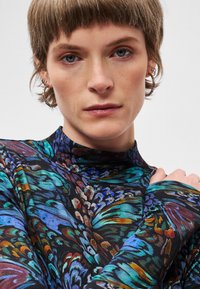 Langärmliges Oberteil mit einem bunten Blumenmuster in Blau, Grün und Orange auf schwarzem Hintergrund, mit hohem Kragen und weicher Textur.