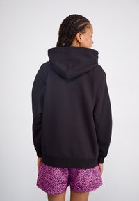 Black cotton hoodie featuring a large hood and relaxed fit, paired with pink leopard print shorts. Smooth texture, casual design.