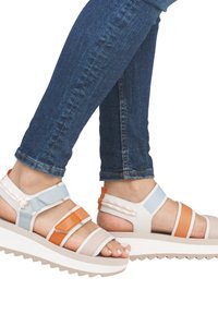 Sandales à lanières présentant un mélange de matériaux blancs, oranges et bleus. Semelle blanche épaisse avec un motif en zigzag. Design ouvert à l'avant qui met en valeur des ongles vernis.