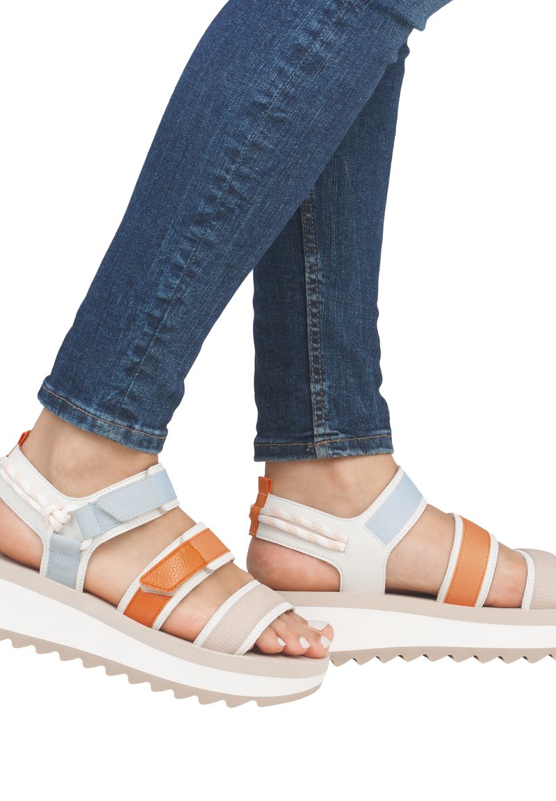 Sandales à lanières présentant un mélange de matériaux blancs, oranges et bleus. Semelle blanche épaisse avec un motif en zigzag. Design ouvert à l'avant qui met en valeur des ongles vernis.