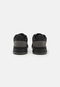 Chaussures de sport noires et grises avec une tige texturée, un col rembourré et une semelle en caoutchouc robuste. Motif géométrique subtil sur le talon.