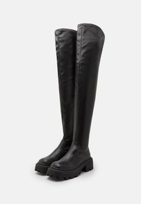 Botas negras altas sobre la rodilla hechas de cuero suave con una suela gruesa y texturizada. Presenta un caña alta y un diseño aerodinámico sin adornos.