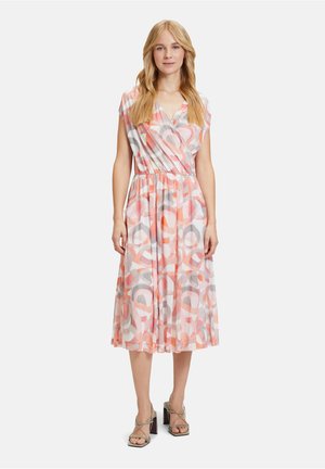 Maxikleid mit Wickeldesign, das eine pastellfarbene Palette aus rosa und grauen Kreisen auf einem transparenten Stoff zeigt. Elastischer Taillenbund und kurze Ärmel.