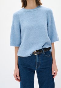 Ljusblå kortärmad tröja i mjukt tyg, med rund hals och lös passform, tillsammans med mörkblå jeans och ett svart bälte.