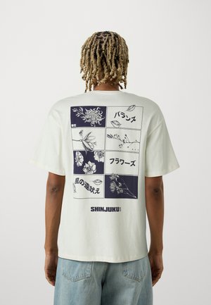 Light cream oversized t-shirt featuring a floral graphic print in navy on the back, with Japanese text and the word "SHINJUKU" at the bottom.