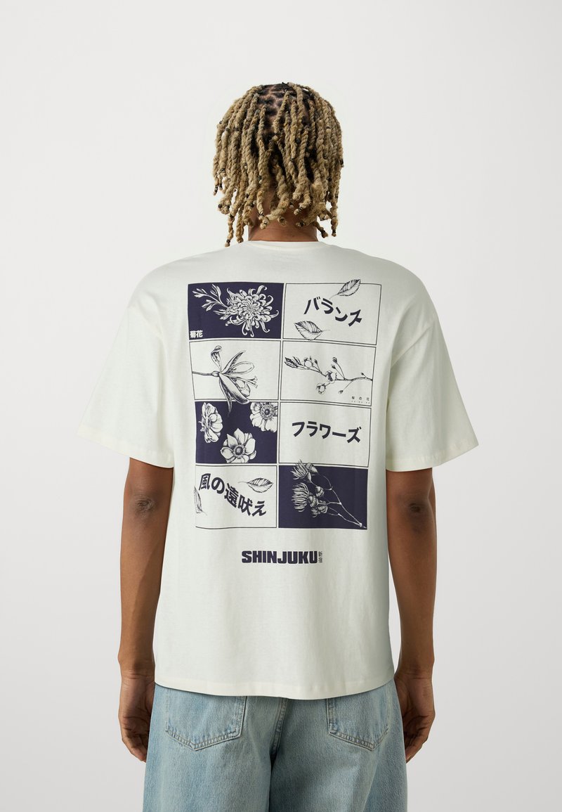 Light cream oversized t-shirt featuring a floral graphic print in navy on the back, with Japanese text and the word "SHINJUKU" at the bottom.