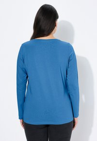 Niebieska bluzka z długim rękawem wykonana z gładkiej tkaniny, z okrągłym dekoltem i luźnym krojem, z gładkim tyłem.