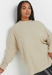 Beige ribbad stickad tröja med hög halsringning, nedsläppta axlar och avslappnad passform. Har långa, smalnande ärmar och mjuk textur.