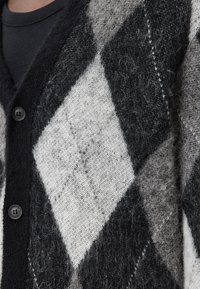 Cardigan en argyle noir et gris, en tissu tricoté doux, avec cinq boutons et une finition texturée.