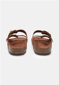 Brown suede sandals with two adjustable straps, a flat cork-like sole, and a textured footbed. Gold-tone hardware accents visible.