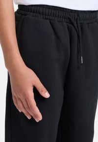 Schwarze Jogginghose aus weichem Stoff mit elastischem Bund, Kordelzug und kleinem Logotag. Verfügt über eine lockere Passform und Seitentaschen.