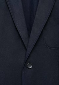 Sacou bleumarin cu un material texturat, rever înclinat, închidere cu un singur buton și un buzunar frontal. Liniile curate și designul minimalist.