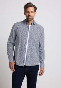 Camicia a maniche lunghe a bottoni blu e bianca con una tasca sul petto, indossata sopra una t-shirt bianca, abbinata a jeans blu.
