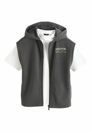 Felpa con cappuccio senza maniche grigio scuro con cerniera, indossata sopra una t-shirt bianca a maniche corte con la scritta "SUBSCRIBE Los Angeles" sul petto.