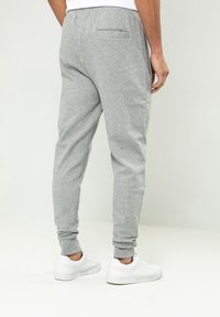 Grå sweatpants lavet af blødt stof, med en tapered ben design, ribbede manchetter og en baglomme. Parret med hvide sneakers.