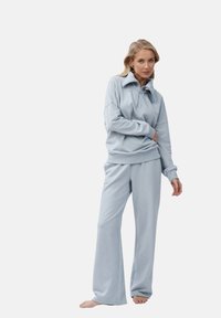 Lichtblauwe trainingsoutfit van zacht materiaal, met een ritssluiting bij de kraag, een ontspannen pasvorm, lange mouwen met geribbelde manchetten en een broek met wijde pijpen.