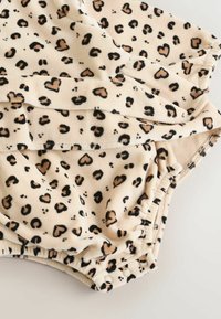 Leopard print fabric featuring black spots and brown hearts on a beige background. Elastic waistband with snap closures at the bottom.