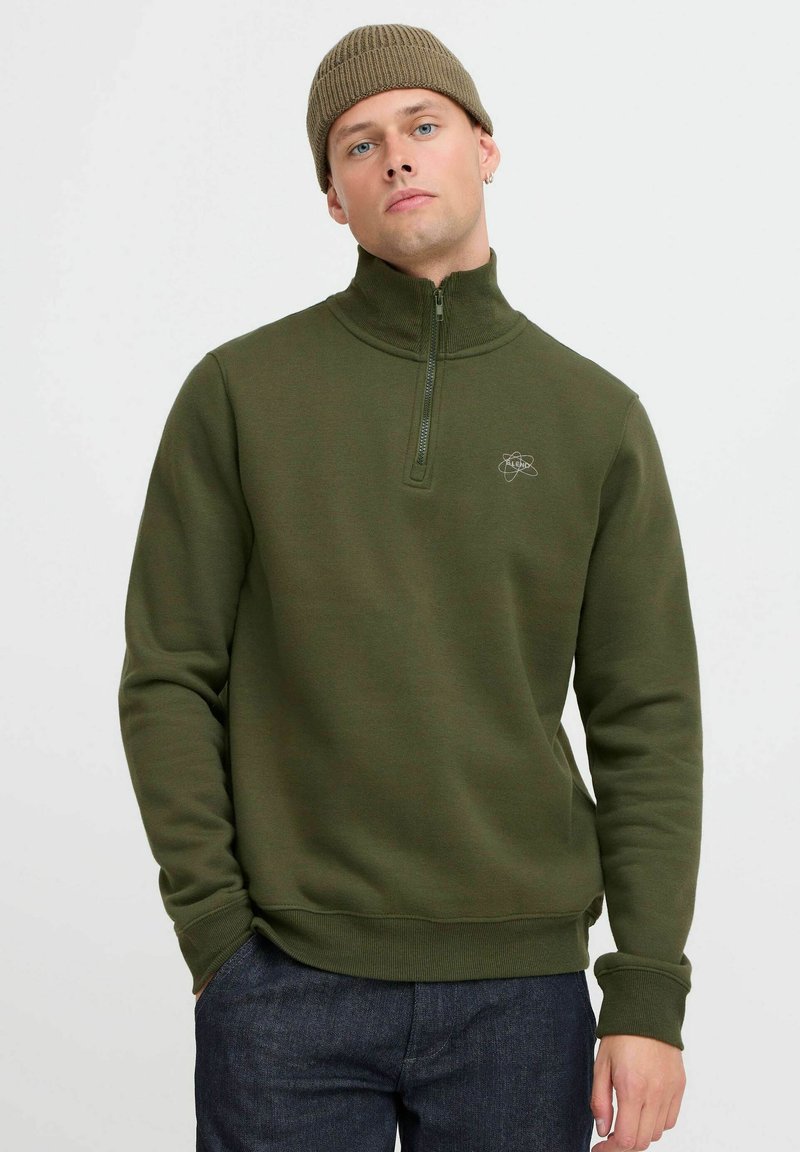 Oliven grønn zip-up sweatshirt med høy krage, ribbestrikkede mansjetter og en liten brodert logo på brystet. Glatt tekstur og tettsittende design.