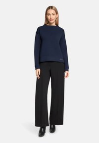 Sweat-shirt bleu marine à coupe décontractée, col côtelé et épaules tombantes, associé à un pantalon noir taille haute à jambes larges.