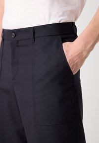 Navy blue trousers made from smooth fabric; features a button closure, slanted front pockets, and a tailored fit.