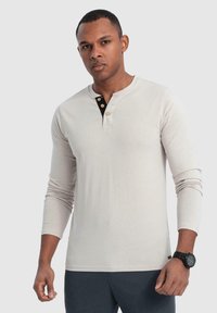 Hellbeige Langarm-Henley-Shirt mit rundem Ausschnitt und dreiknöpfiger Knopfleiste, versehen mit schwarzen Akzenten. Weicher, glatter Stoff.