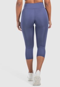 Leggings capri blu navy realizzati in tessuto elastico, con vita alta e texture liscia, abbinati a scarpe da ginnastica bianche.
