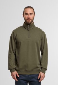 Pullover verde oliva con zip e collo alto, realizzato in un tessuto morbido e con vestibilità comoda. I polsini e l'orlo a costine conferiscono struttura.