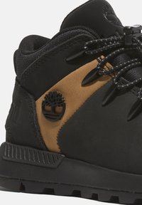 Chaussures de randonnée noires et beiges présentant un dessus texturé, un col rembourré, un talon durable et des éléments en métal noir avec un accent logo d'arbre.