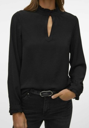 Zwarte blouse met lange mouwen, keyhole-halslijn en gerimpelde manchetten, gecombineerd met zwarte spijkerbroek en een zwarte riem met zilveren gesp.