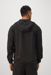 Schwarze Kapuzenjacke aus glattem, leichtem Material. Verfügt über elastische Bündchen und eine Kordelzugkapuze. Einfaches, funktionales Design ohne sichtbare Logos.