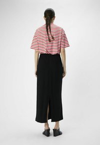 T-shirt surdimensionné rayé rouge et blanc associé à une jupe noire longueur cheville avec une fente arrière et une taille élastique. Chaussures à talons noires.