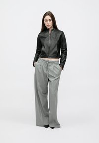 Black leather cropped jacket with a zip front, paired with light gray, wide-leg trousers featuring a drawstring waist.