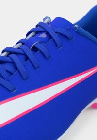 Μπλε αθλητικό παπούτσι με ταιριαστά κορδόνια, λεπτομέρειες σε λευκό και ροζ ρίγα, και ροζ καρφιά ορατά στη σόλα.