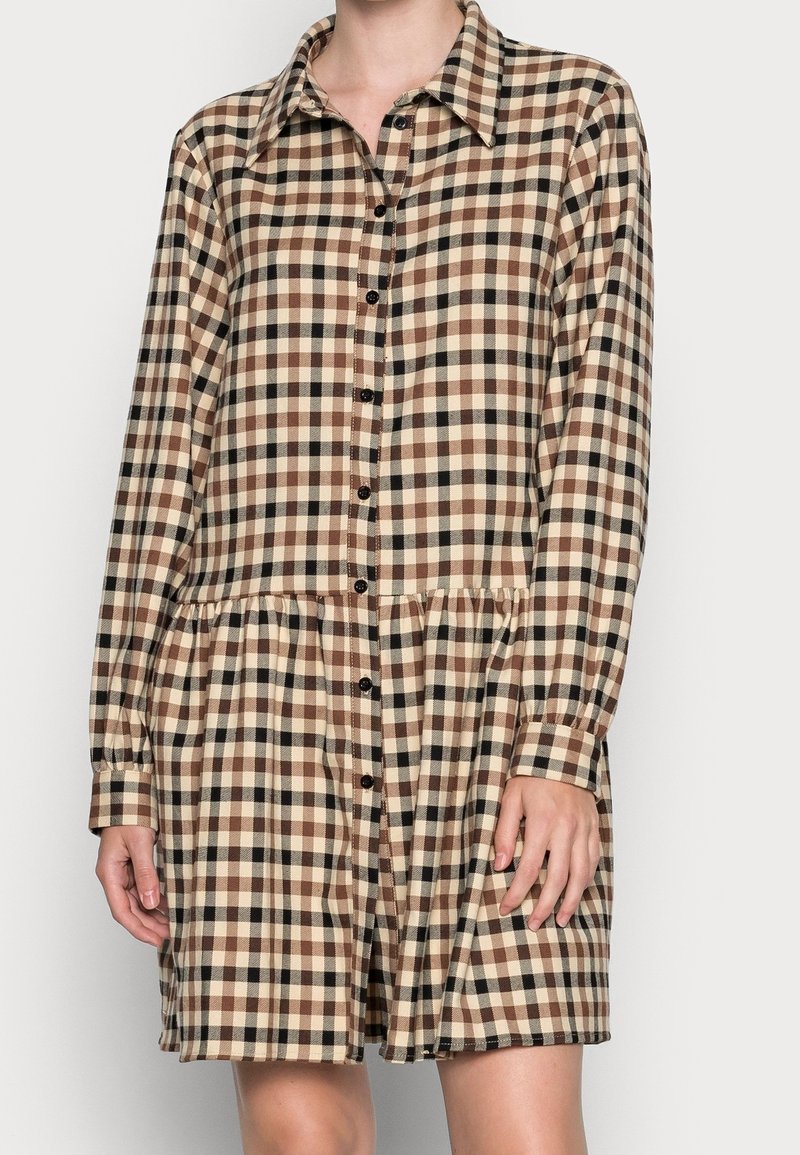 Robe à carreaux avec un devant boutonné, des manches longues et un ourlet à volants. La palette de couleurs comprend du beige, du marron et du noir.