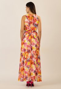 Blumenmaxikleid mit leuchtend pinken, gelben und blauen Mustern. Ärmelloses Design mit tailliertem Bund und fließendem Stoff. Kombiniert mit pinken High Heels.