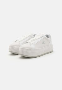 Hvite plattform-sneakers i teksturert lær med glatte detaljer, med flate lisser, en logo på siden og såle med riller.