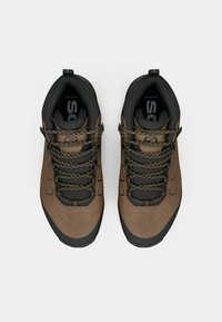 Zapatos de senderismo marrones con parte superior de ante texturizado, acentos negros y cordones amarillos con motas, que cuentan con un collar acolchado para mayor comodidad.