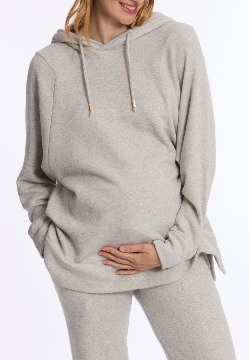 Lichtgrijze hoodie gemaakt van zachte stof, met een voorzak, trekkoorden en een relaxte pasvorm. Gecombineerd met bijpassende grijze broek.