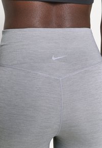Zbliżenie na osobę w szarych legginsach sportowych o wysokim stanie z logo Nike na pasku.