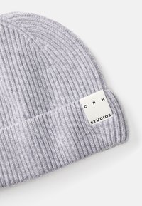 Căciulă din tricot gri cu nervuri, prevăzută cu un tiv pliat. Are o etichetă rectangulară cu "CPH STUDIOS" imprimat cu negru pe un fundal alb.