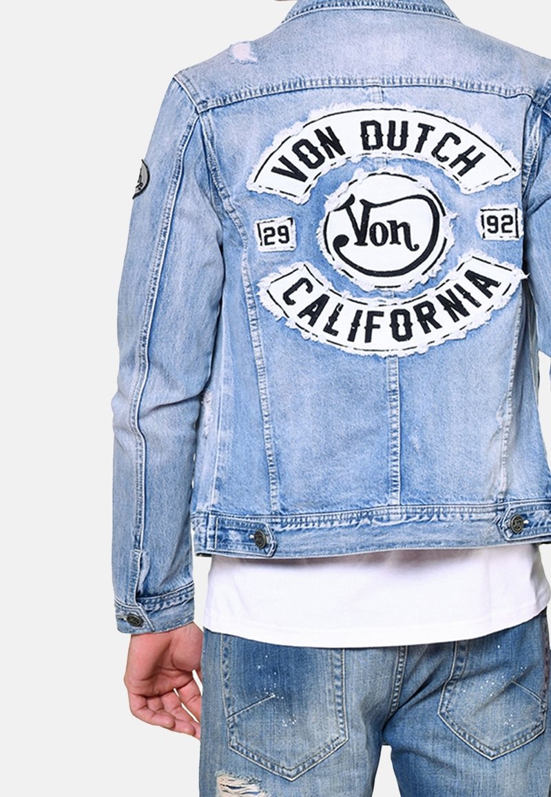 Ljusblå denimjacka med en sliten baksida där "Von Dutch California" är broderad i svart och vitt, knäppta ärmar och en figurnära design.